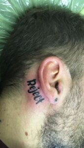 Tatuaje de tipografia detrás de la oreja hombre